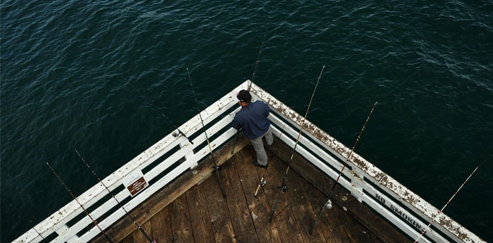 Photo of man fishing from a pier with multiple rods